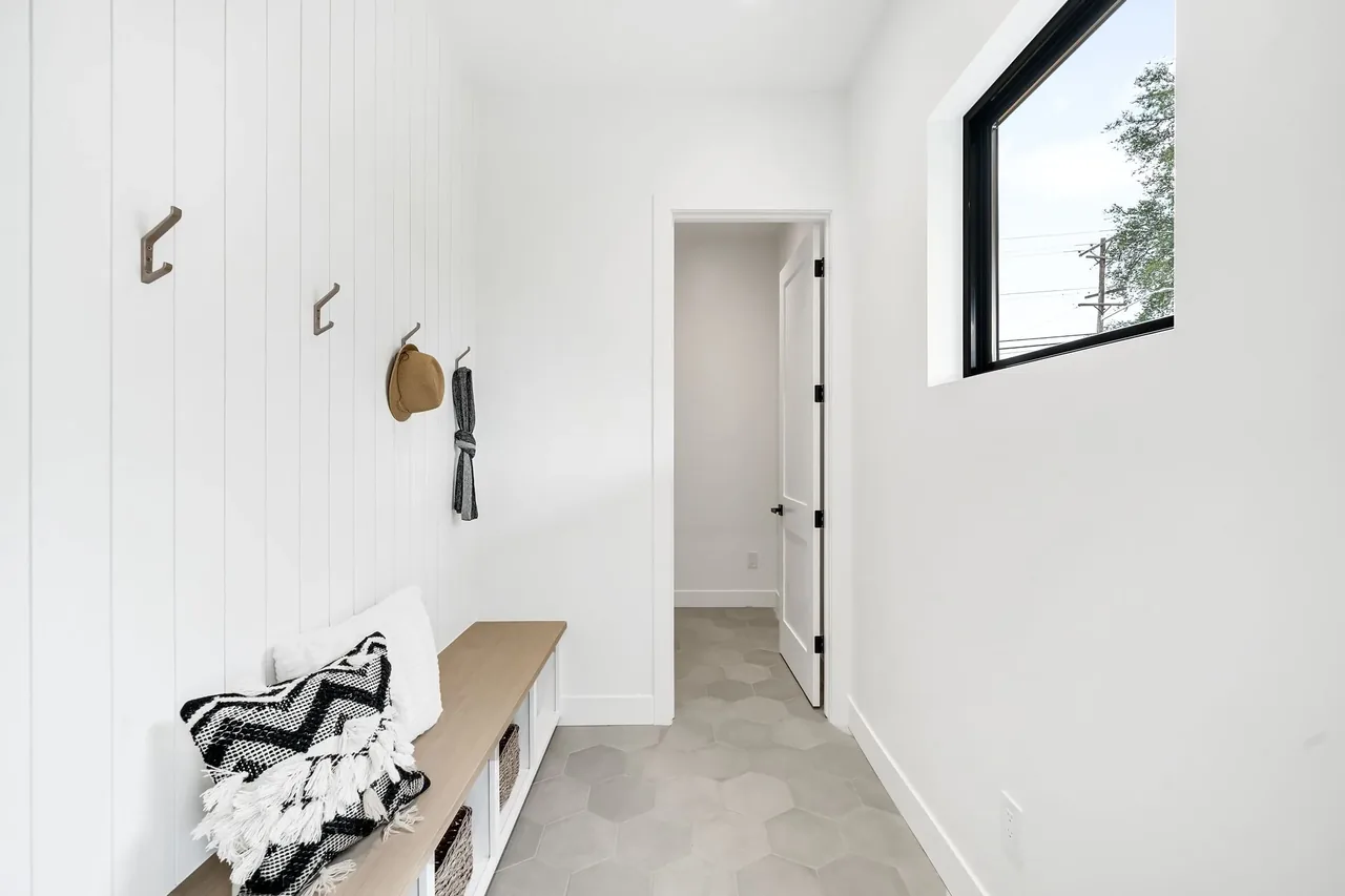 Mudroom featuring a wooden bench with woven baskets, white vertical shiplap walls, hexagonal tile floor, and a black-framed window.