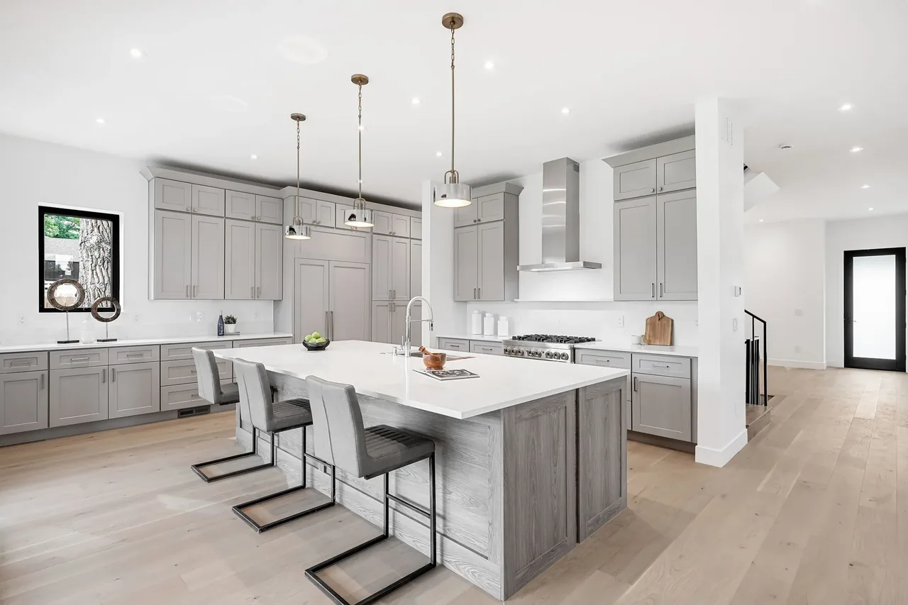 Kitchen with gray cabinets, a central island with three chairs, and pendant lighting.