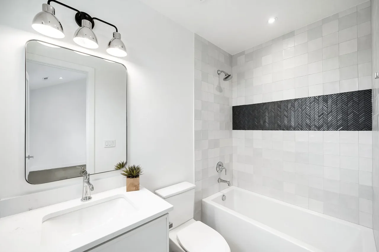 Bathroom features white and gray tile with a black herringbone accent strip and a white vanity with framed mirror.