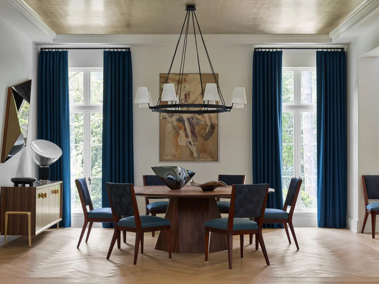 Dining room features a round wood table with blue chairs, large tall windows with blue curtains, and a chandelier overhead.
