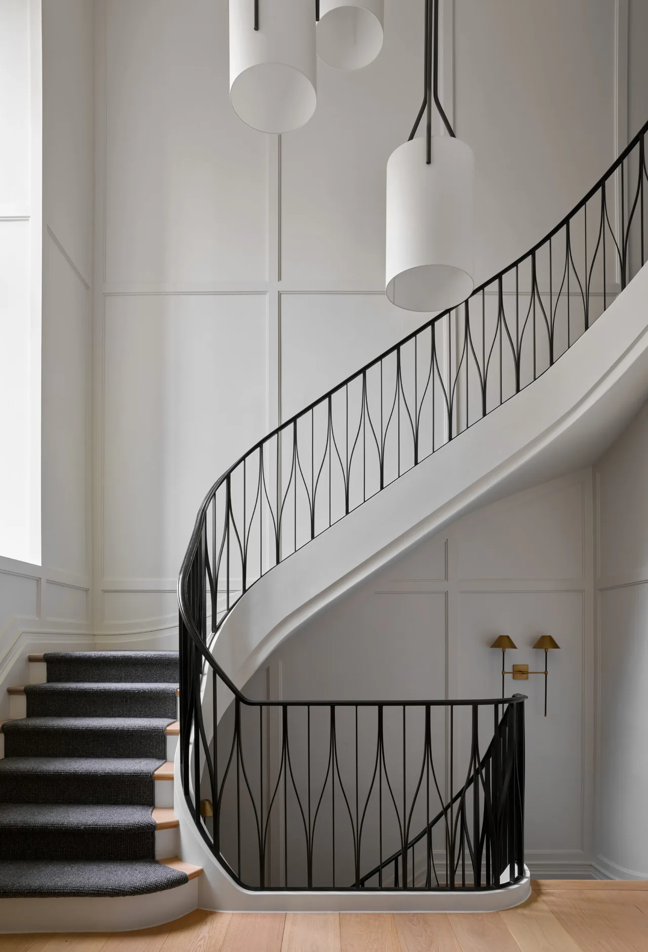 A modern curved staircase with decorative black metal railing and carpeted treads in a white paneled entry space.