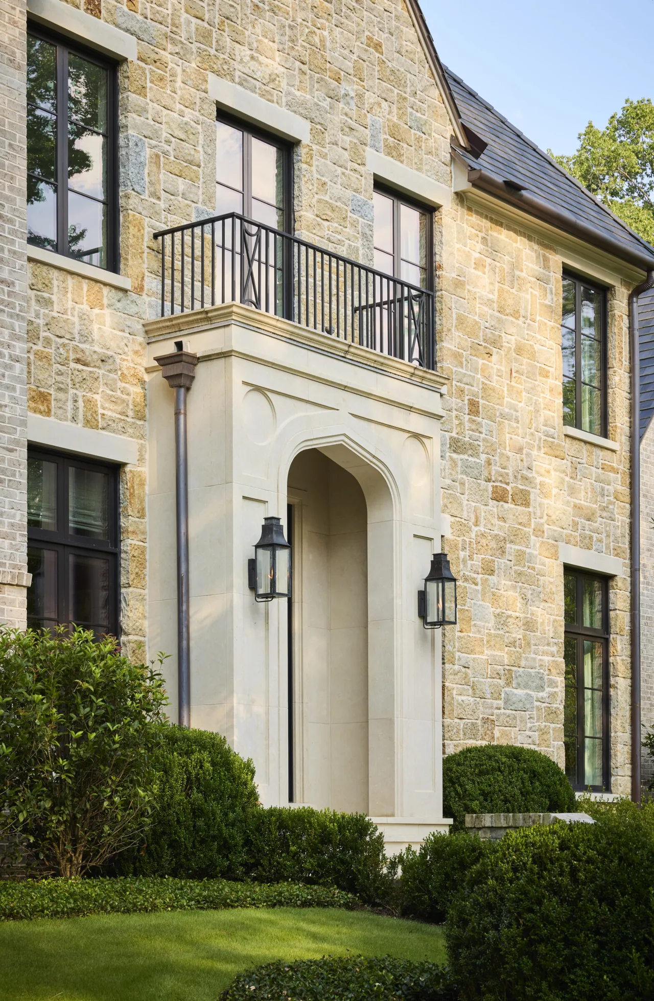 Front exterior of the Modern English Manor showing stone siding, steep gable roof, and arched entryway with balcony.