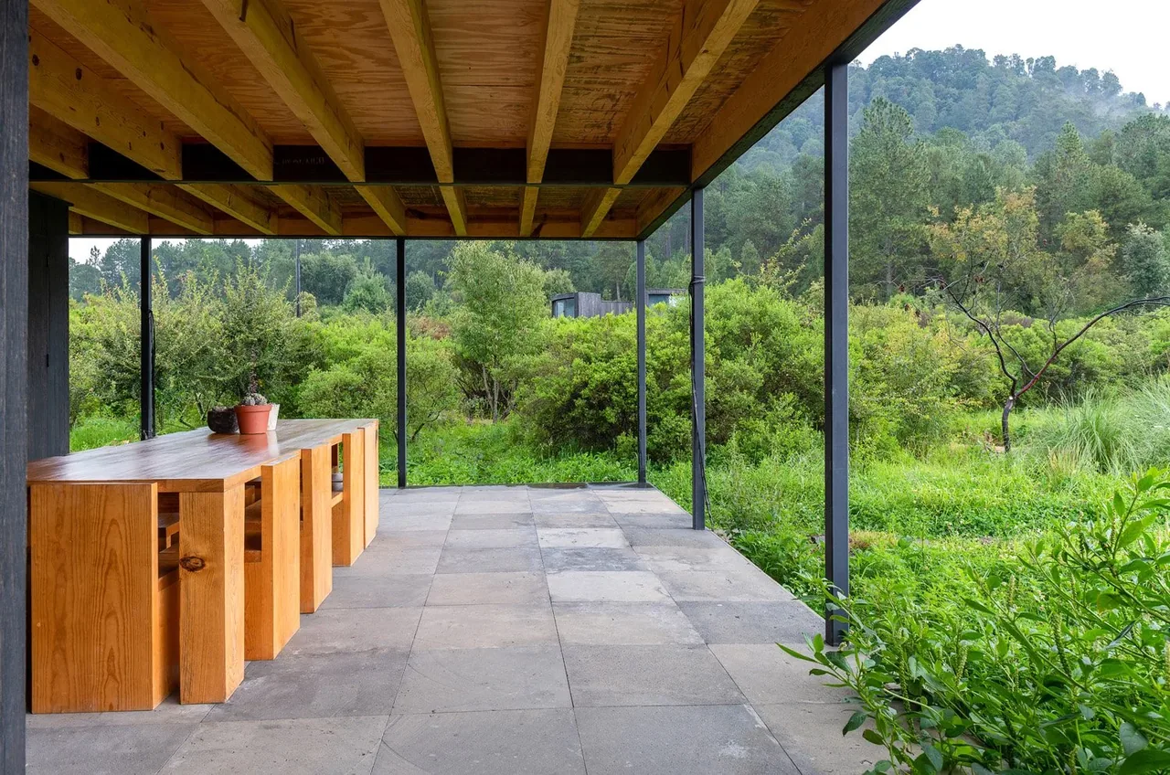 The outdoor patio of Casa Temascaltepec features a wooden dining table with stools under a covered roof with exposed beams, overlooking a natural landscape.