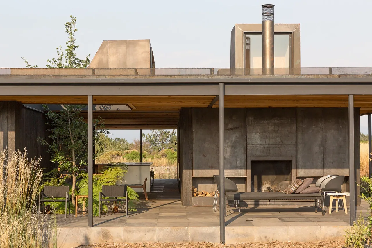 Outdoor living area of Casa Temascaltepec featuring a metal fireplace, seating, and pergola roof with forest backdrop.