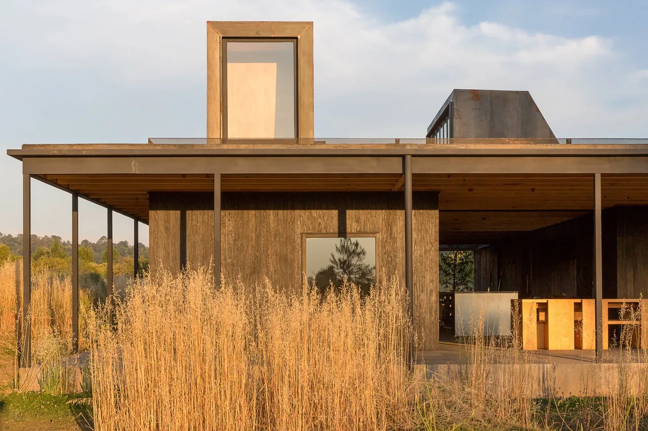 Casa Temascaltepec features rusted metal accents and wood siding with large windows and an overhanging flat roof.