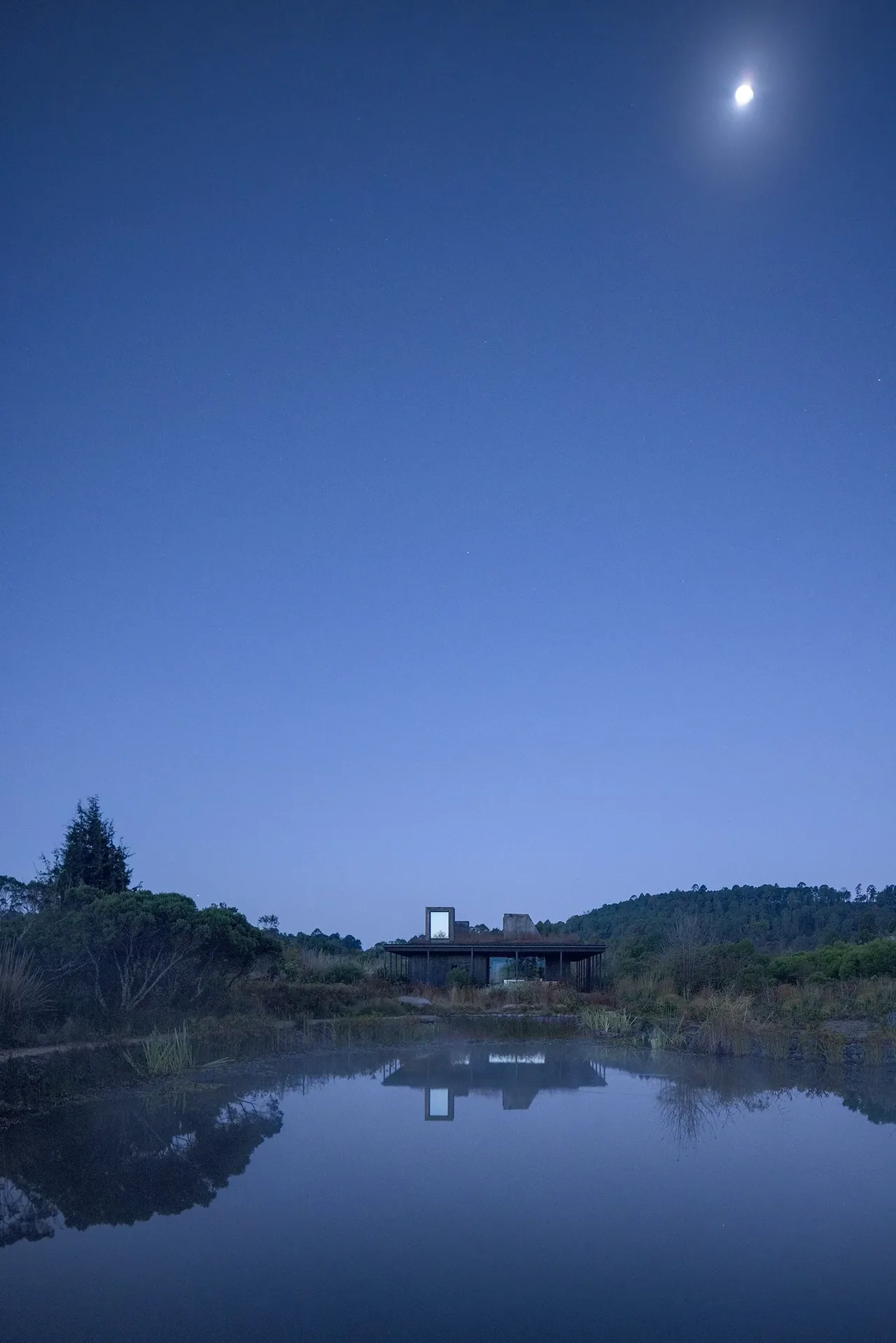 Casa Temascaltepec is a modern home partially surrounded by natural landscape and reflected in a peaceful pond.