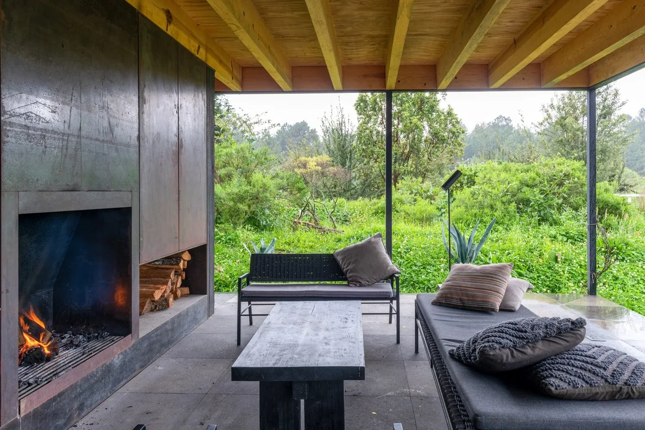 Sheltered patio features a metal fireplace, outdoor seating with cushions, and natural landscape views.