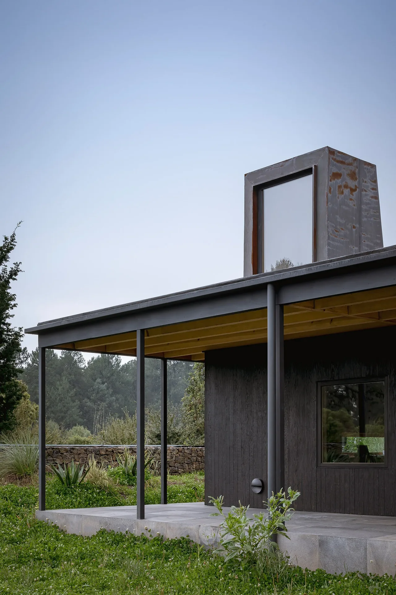 Casa Temascaltepec features dark wood siding, a flat roof, and a covered patio set in a natural landscape.
