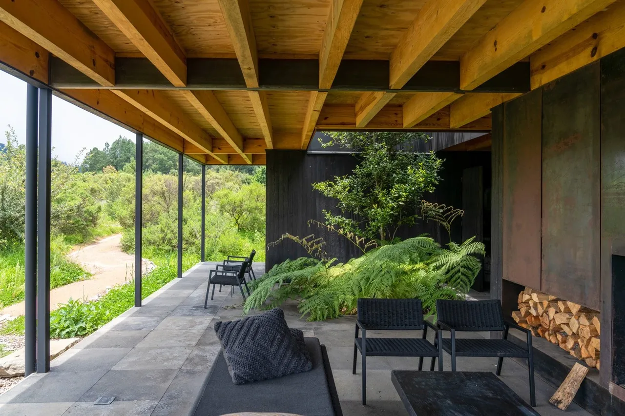 Covered patio at Casa Temascaltepec shows exposed wood beams, metal fireplace enclosure, and natural landscaping views.