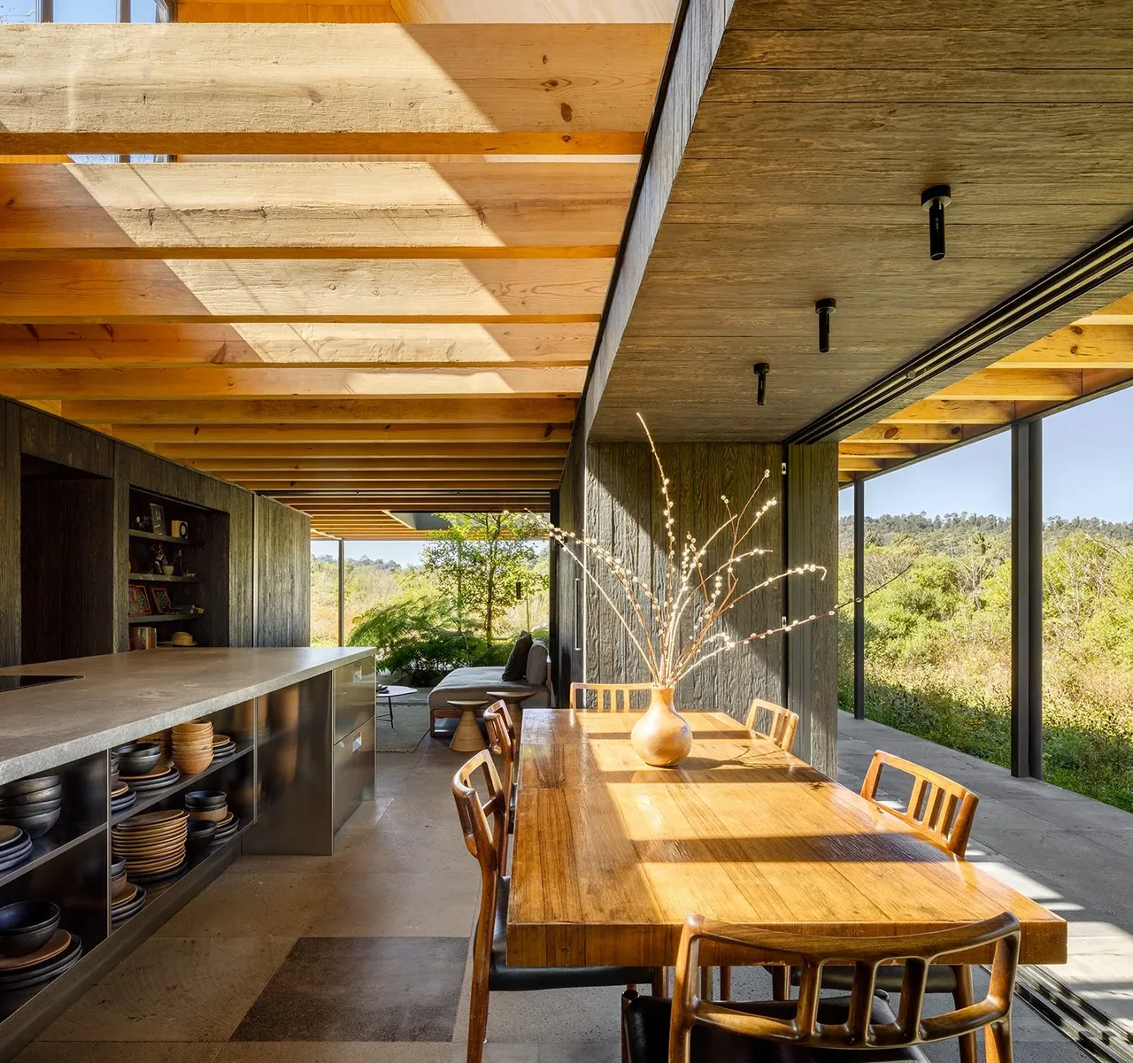 Dining area adjacent to kitchen with open sliding glass doors showing lush landscape outside.