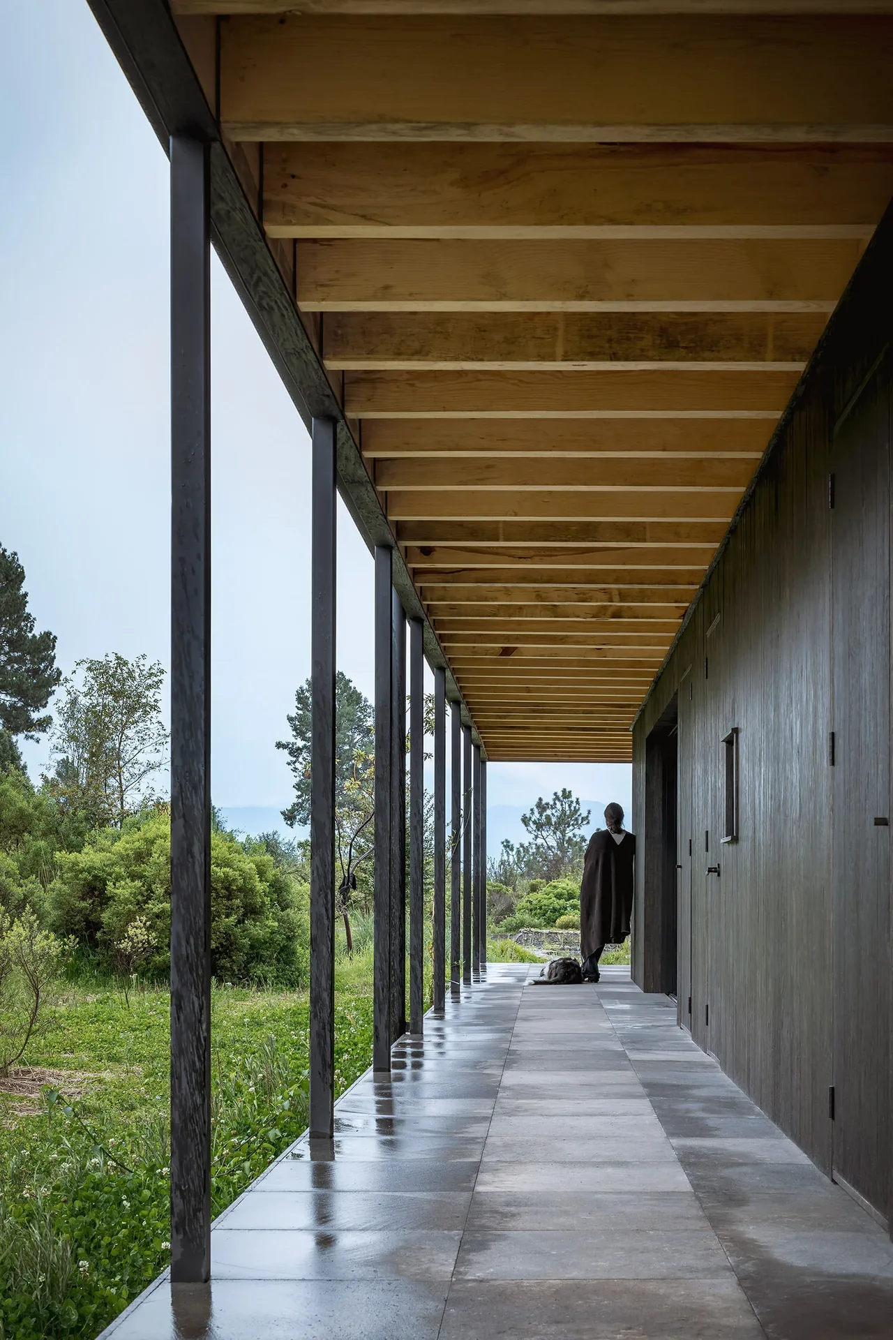 Sheltered patio at Casa Temascaltepec features exposed wood beams, black metal supports, and a concrete tile floor with a green landscape beyond.