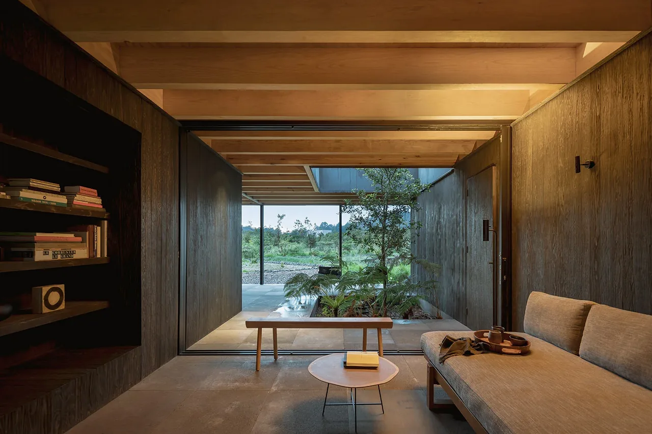 Living area with exposed wood beams overlooking an indoor garden and natural landscape beyond.