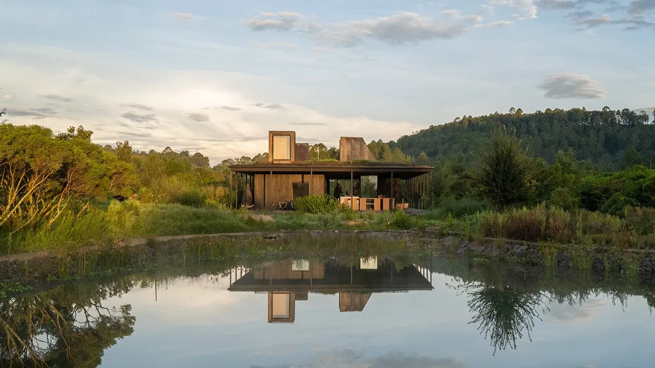 Casa Temascaltepec features a flat-roof modern design with large glass walls overlooking a natural pond and forested hills.