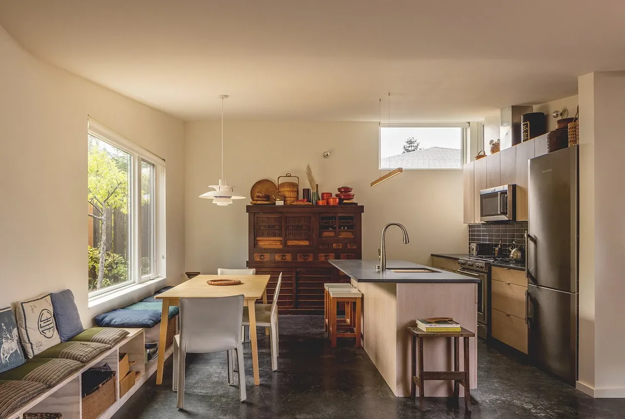 Kitchen and dining area in House O features a kitchen island with sink, built-in bench seating, and a vintage cabinet.