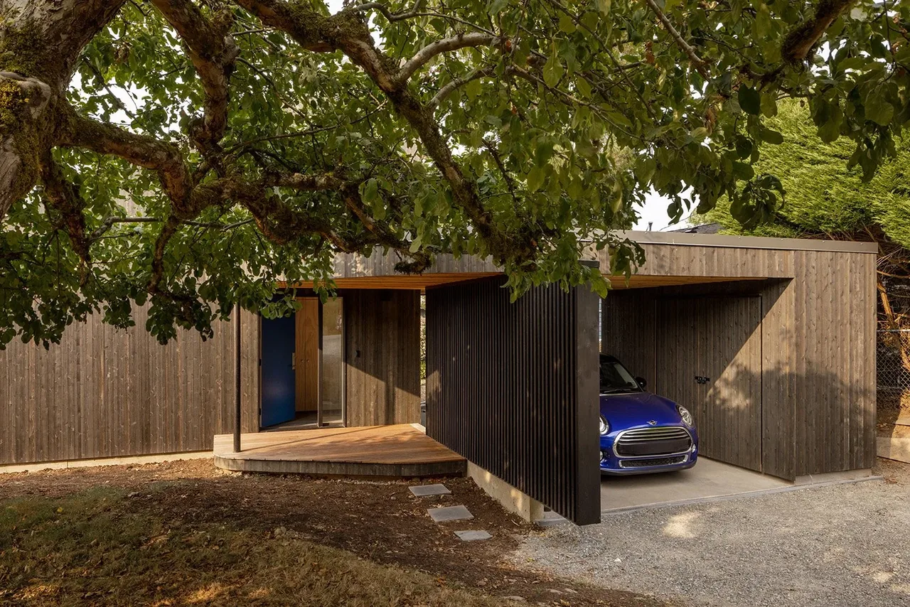 House O exterior with wood siding and a carport showing a blue car, designed by Hutchison & Maul Architecture in Seattle.