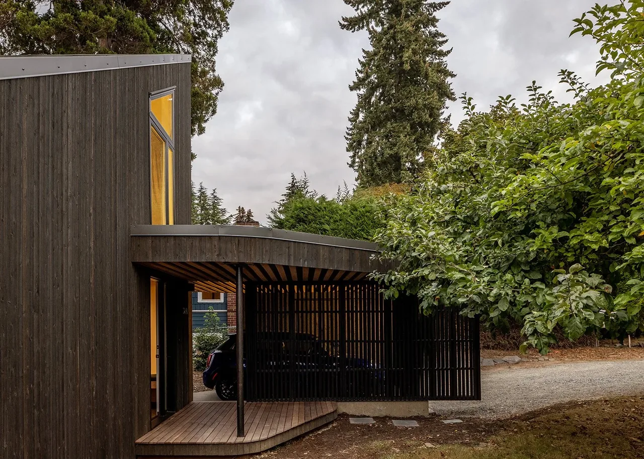 House O features dark wood siding and a carport with vertical slats beside a wood deck entry under a sloped roof.