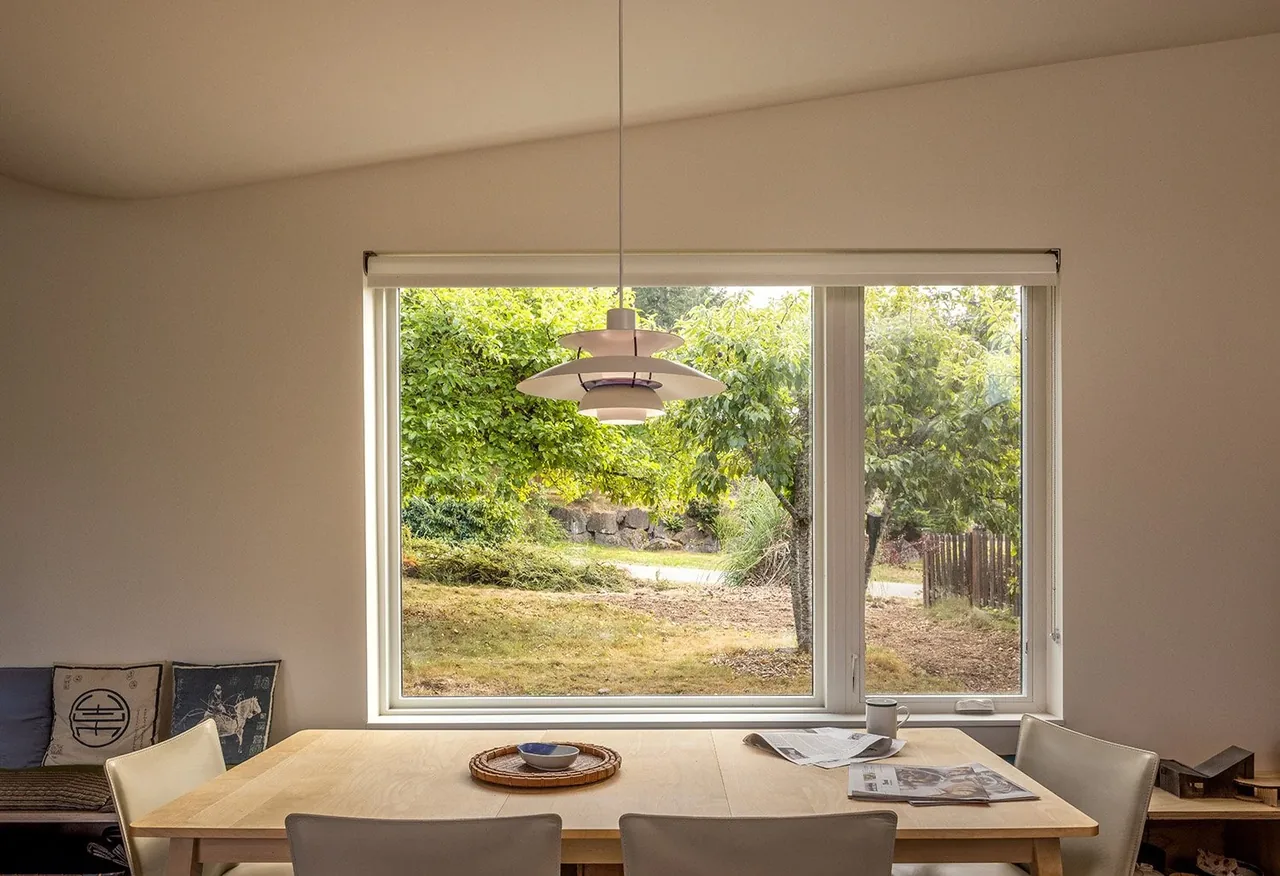 Dining room with large window providing views of greenery outside and a modern pendant light hanging above the table.