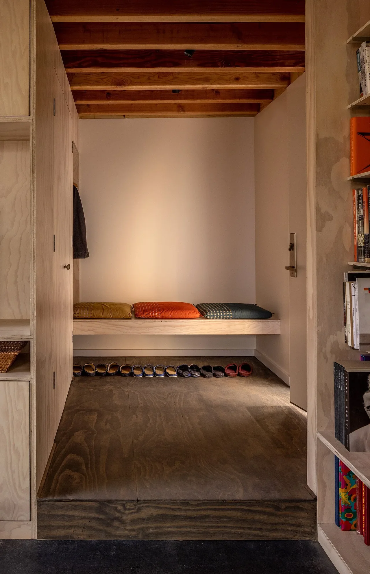 Minimalist entry with built-in bench and shoe storage beneath, showcasing exposed wood ceiling beams.