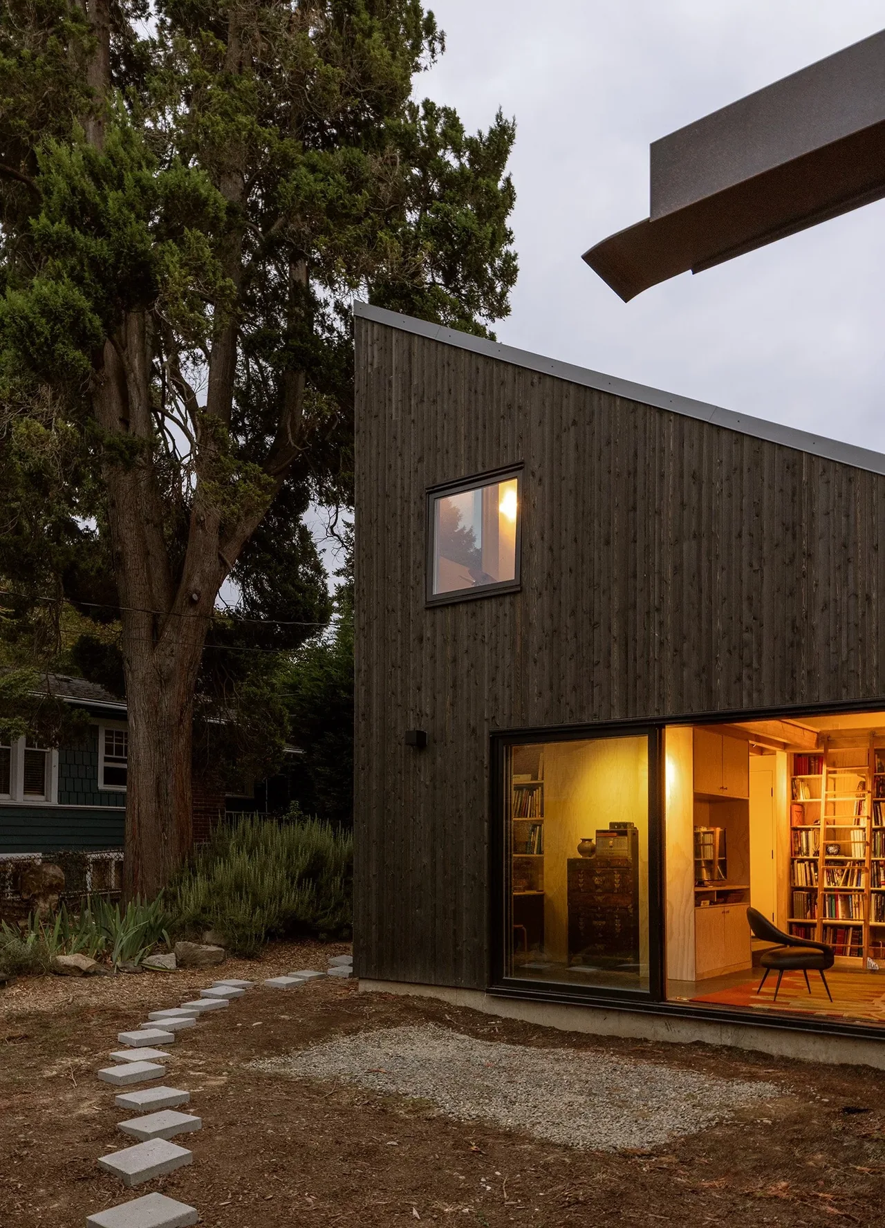 House O features dark wood siding, a sloped roof, and large glass windows that frame the warmly lit interior with bookshelves.