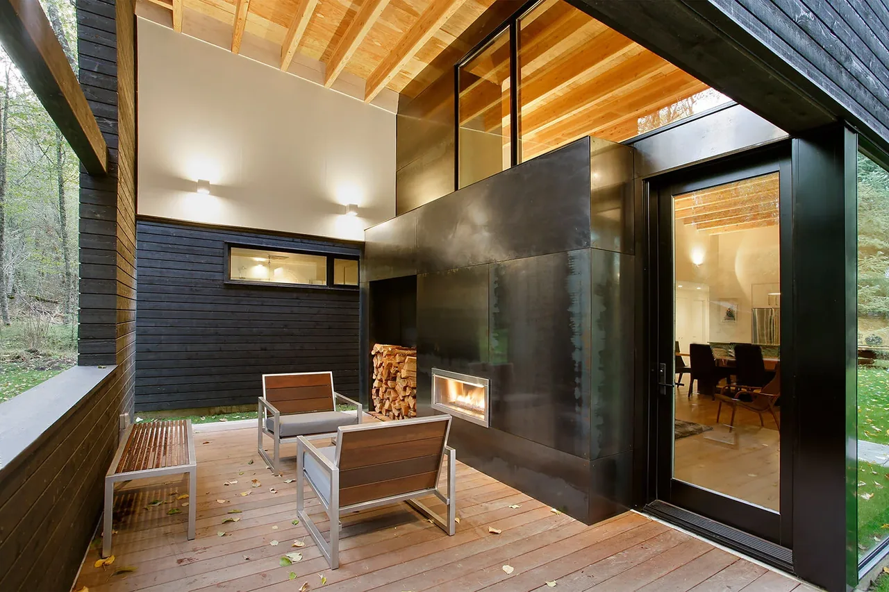 Covered patio with metal fireplace wall and seating opens to the forest setting of the Courtyard House on a River project.