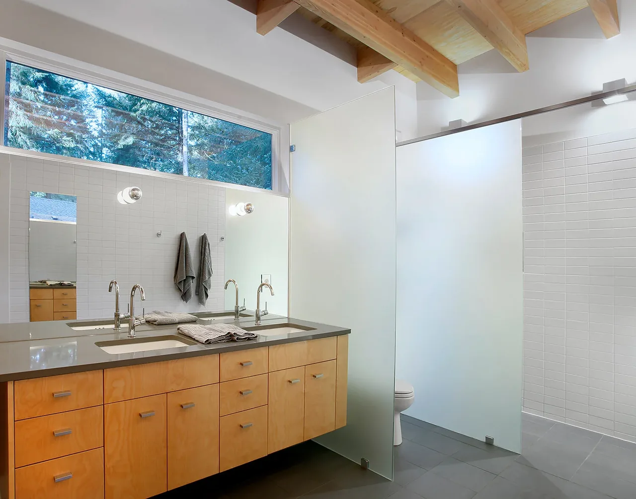 Bathroom featuring a double vanity with wood cabinets and a frosted glass privacy partition.