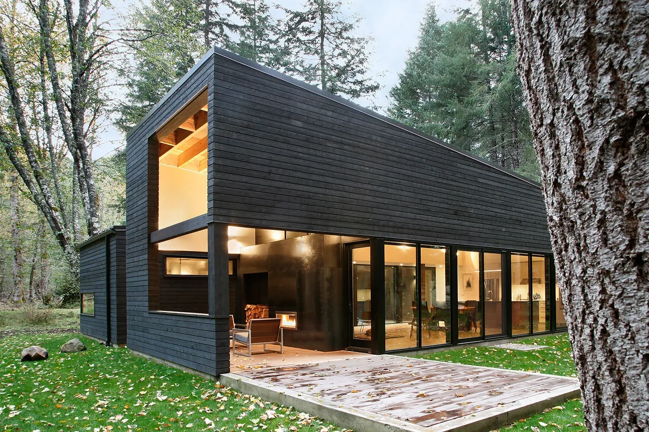 The Courtyard House on a River features dark wood siding, large windows, and a covered patio with integrated fireplace.