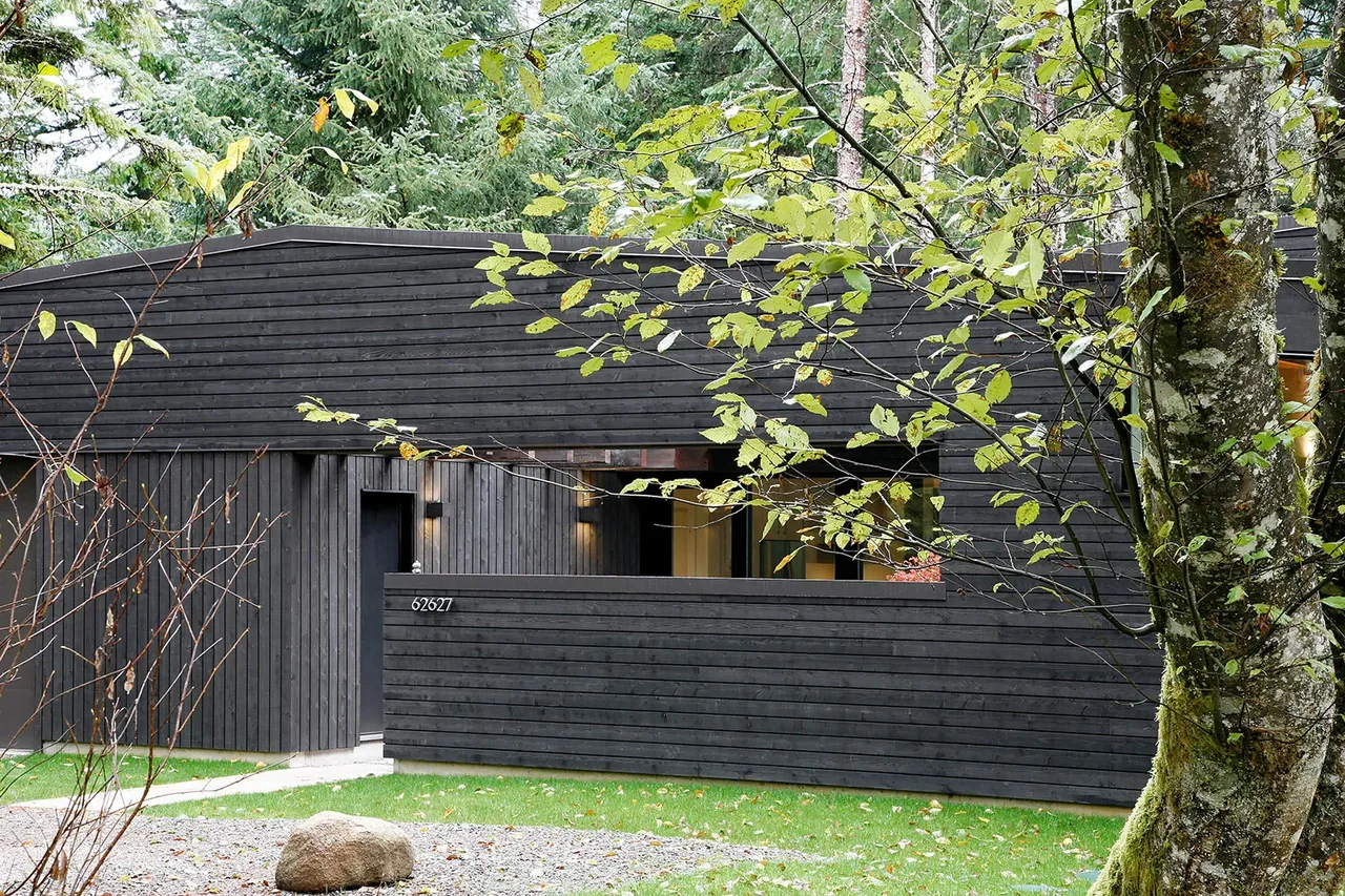 The front entrance of the Courtyard House on a River features dark horizontal wood siding with a low fence and a sloped roof.