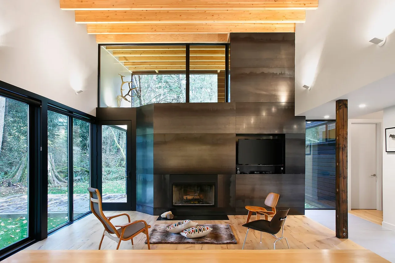 The living room features a prominent metal fireplace wall, large glass doors opening to the outdoors, and exposed wood ceiling beams.
