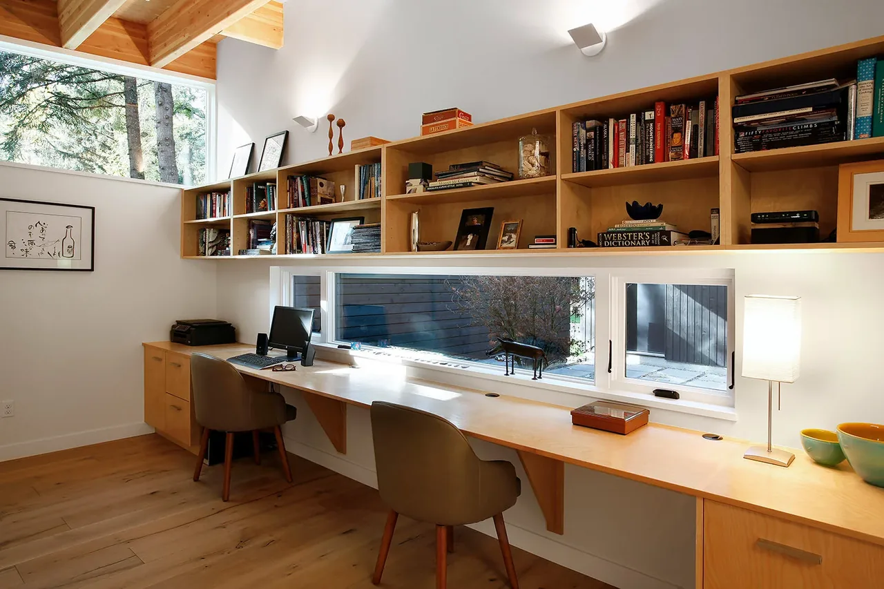 Home office features a built-in wooden desk and shelving with ample natural light from clerestory and horizontal windows.