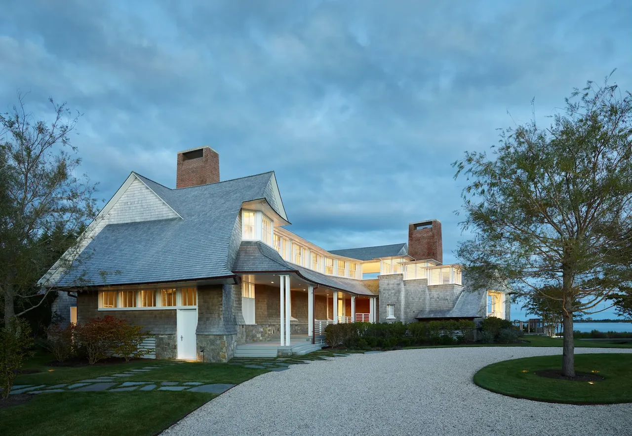 Water Mill House by KLIGERMAN ARCHITECTURE features wood shingle siding, steep roof, and brick chimneys near a water view.
