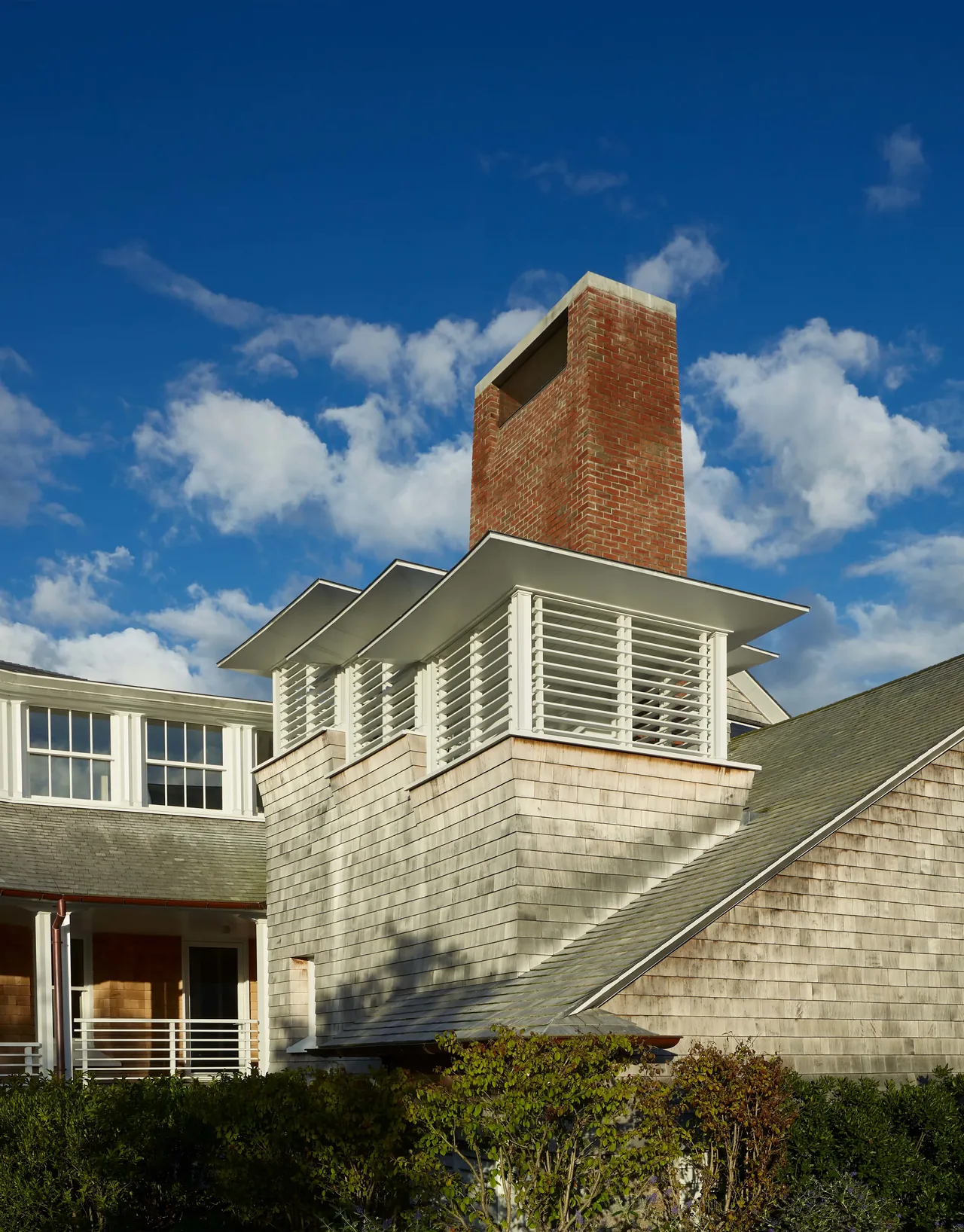 Chimney with red brick and white horizontal slats rising above a shingled roof and siding.