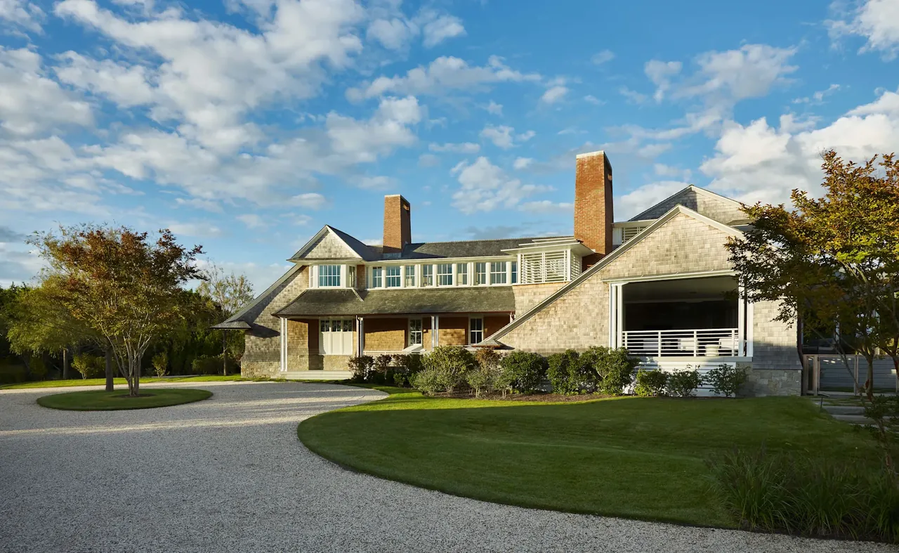 Water Mill House by KLIGERMAN ARCHITECTURE features shingle siding and brick chimneys with a circular gravel driveway.