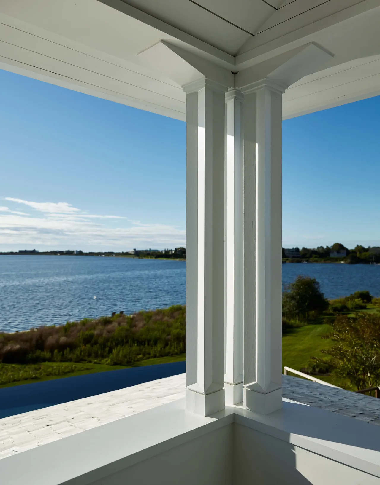 Corner of a white wooden porch with a view of marshland and waterfront in the distance.
