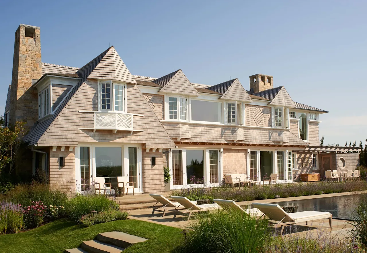 Sagaponack Beach Front Hideaway features shingle siding, dormer windows, and a stone chimney at the rear with a pool and garden area.