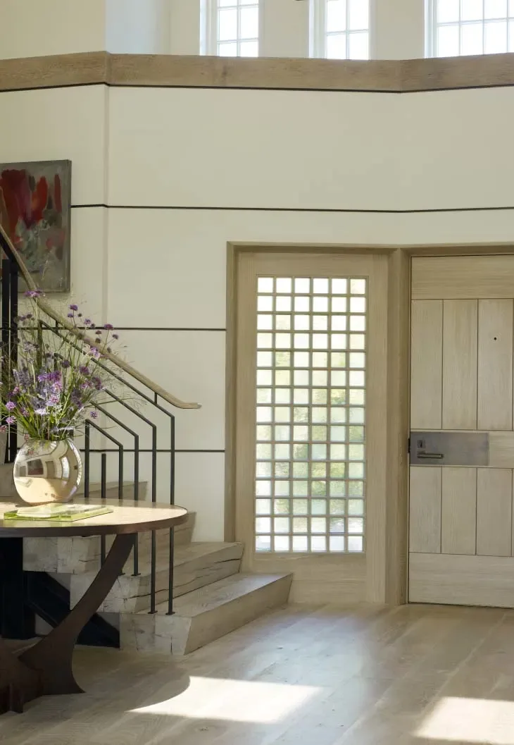 Entry area featuring a wooden door, grid patterned glass sidelights, stone stairs, and a round table with a vase of flowers.