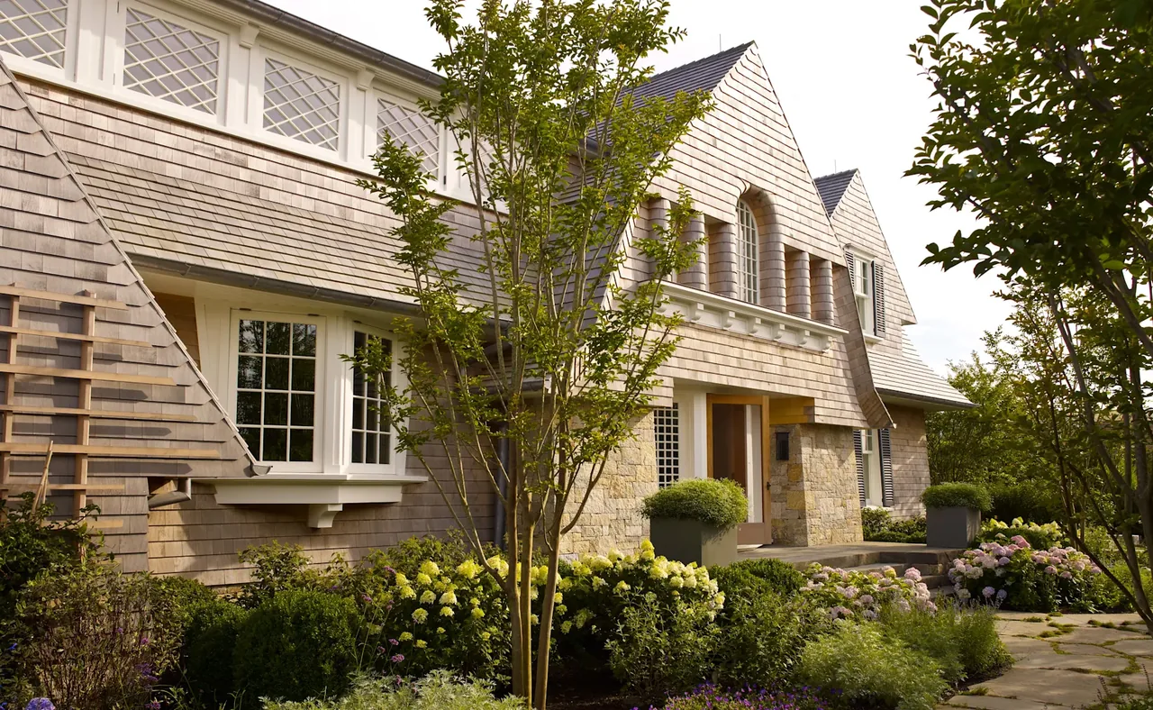 Sagaponack Beach Front Hideaway features shingle siding, stone base, and symmetrical windows with landscaped garden beds.
