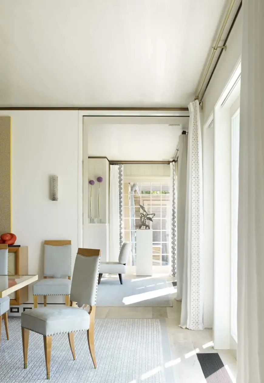 Sagaponack Beach Front Hideaway features a bright interior with upholstered dining chairs and tall windows with white curtains.