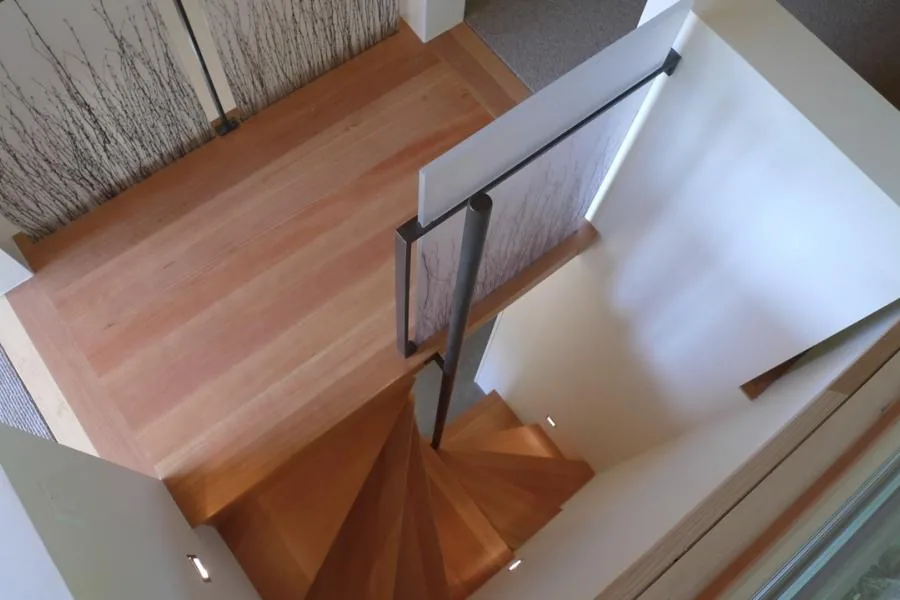 Wooden spiral staircase with metal handrail and decorative glass panel featuring tree branch motifs.
