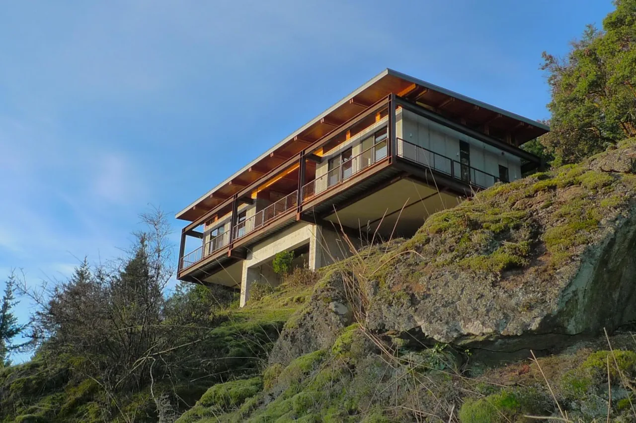 Buck Mountain Weekend house features flat roof and cantilevered design on a hillside with balcony railing.