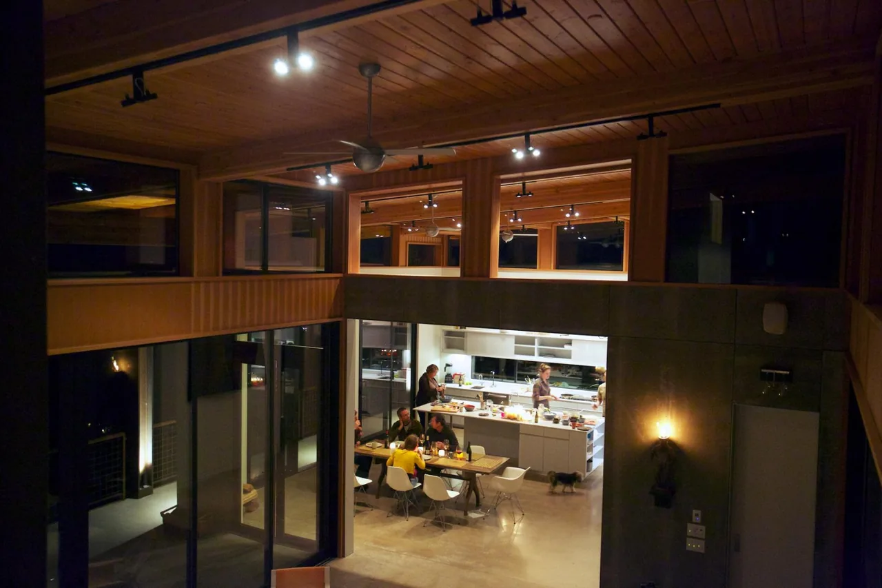 Modern kitchen and dining space with wood ceiling, large windows, and recessed lighting at night.