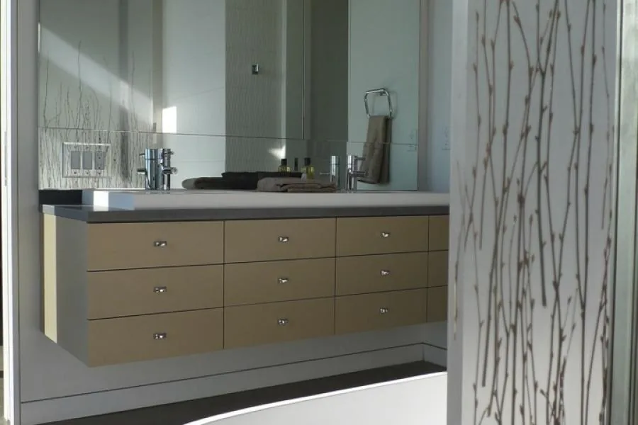 A modern floating bathroom vanity with dual faucets and a large mirror under natural light.