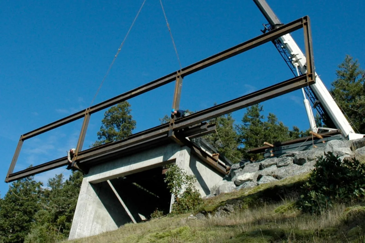 Steel frame installation on a concrete base in a wooded, rocky area.