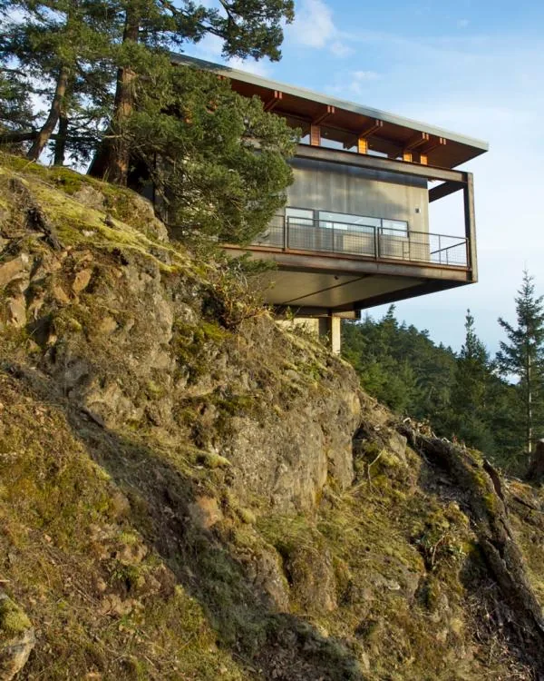 Buck Mountain Weekend house cantilevered on a rocky hillside with flat roof and metal balcony railing.