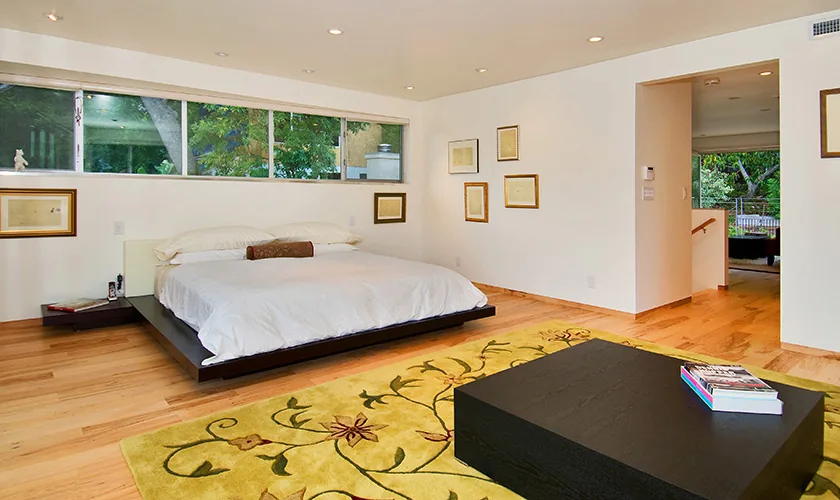 The bedroom features a low platform bed, clerestory window, hardwood floors, and recessed lighting, combining minimalist style with functional simplicity.
