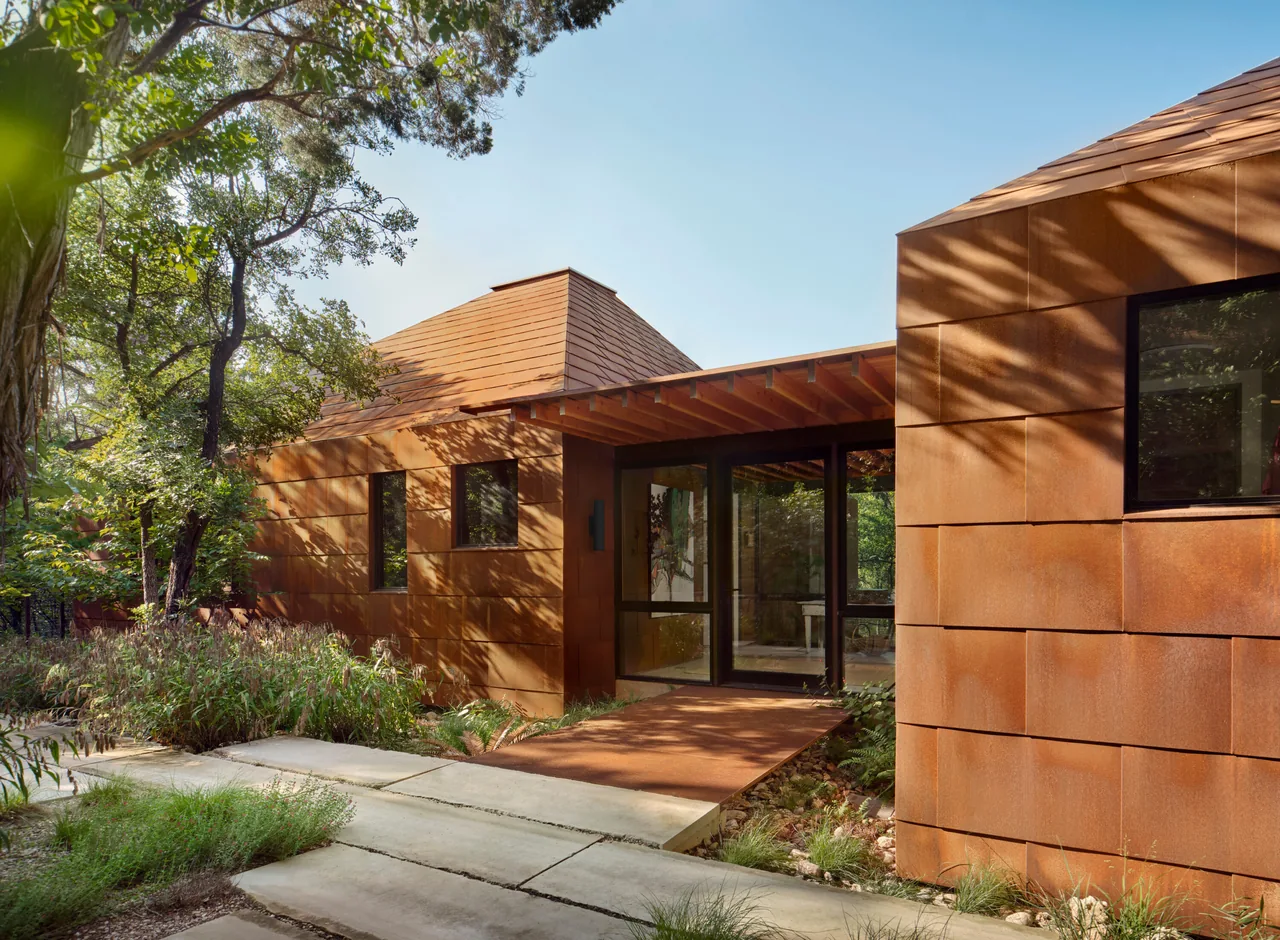River Bend Residence features rust-colored paneled metal exterior with black window frames and a flat roof under natural landscape