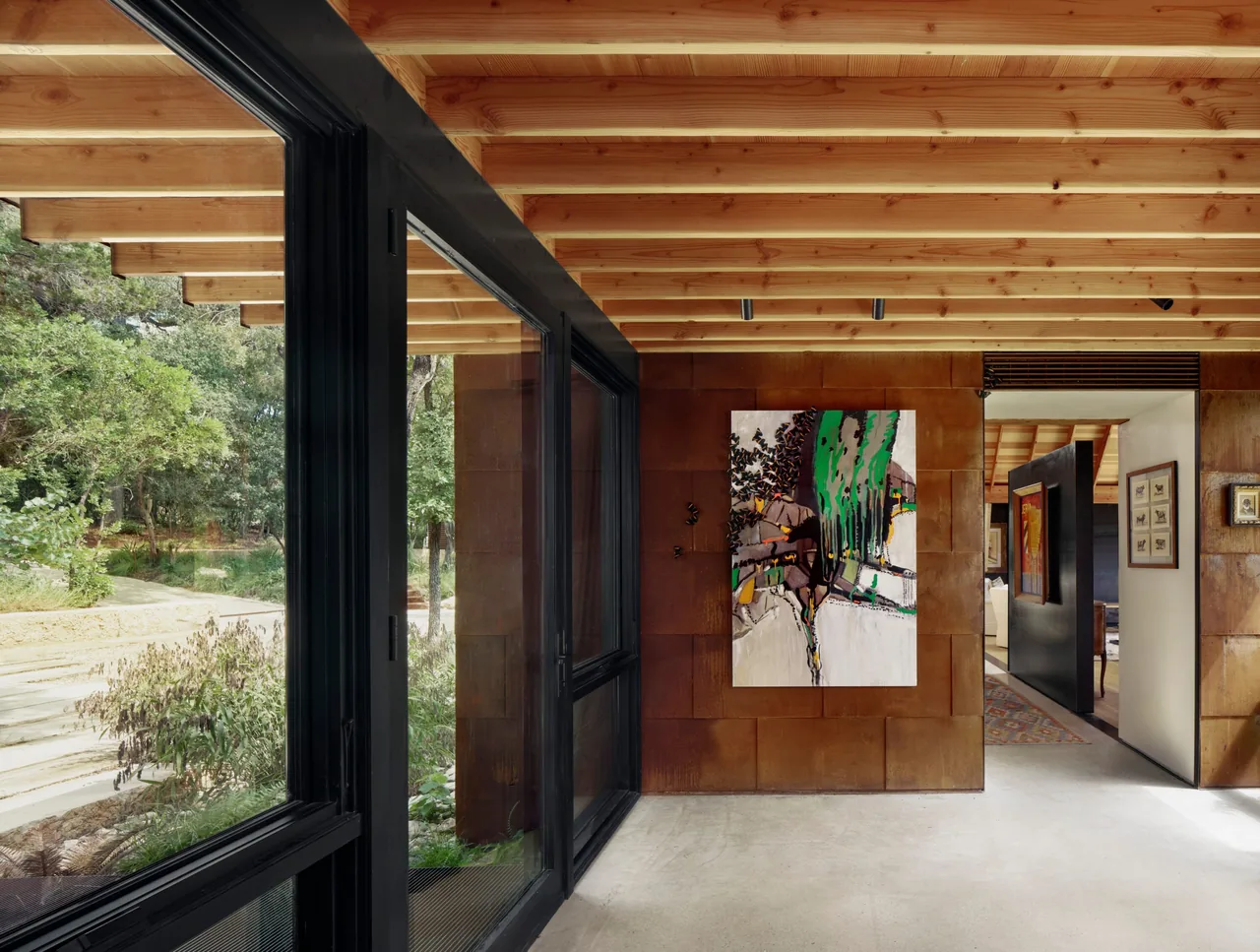 Hallway of River Bend Residence features black window frames, rust colored metal panel siding, and exposed wood beams.