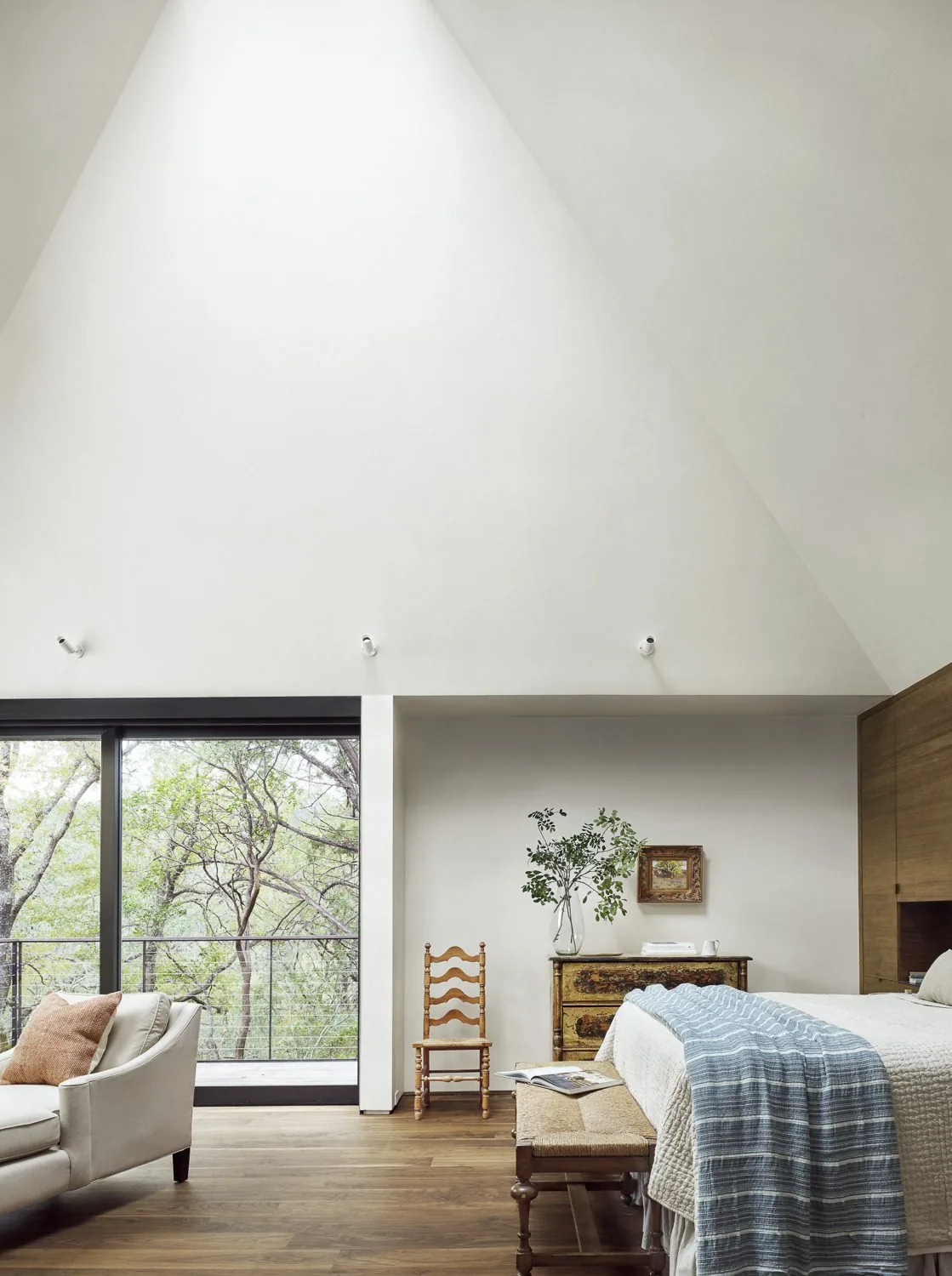 Bedroom with vaulted ceiling and large sliding glass door overlooking natural landscape.