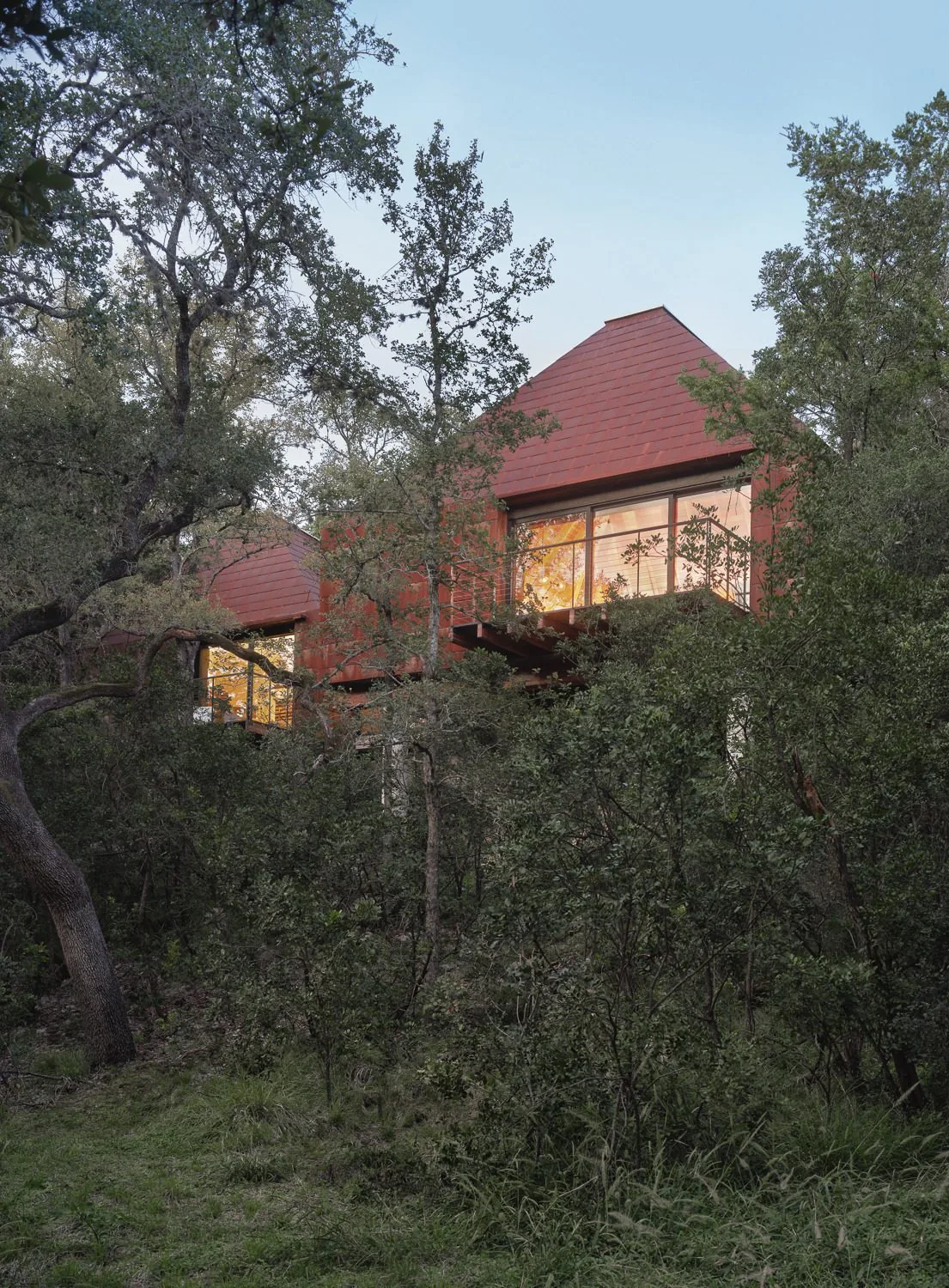 River Bend Residence features rust-colored paneling and large windows surrounded by woodland vegetation.