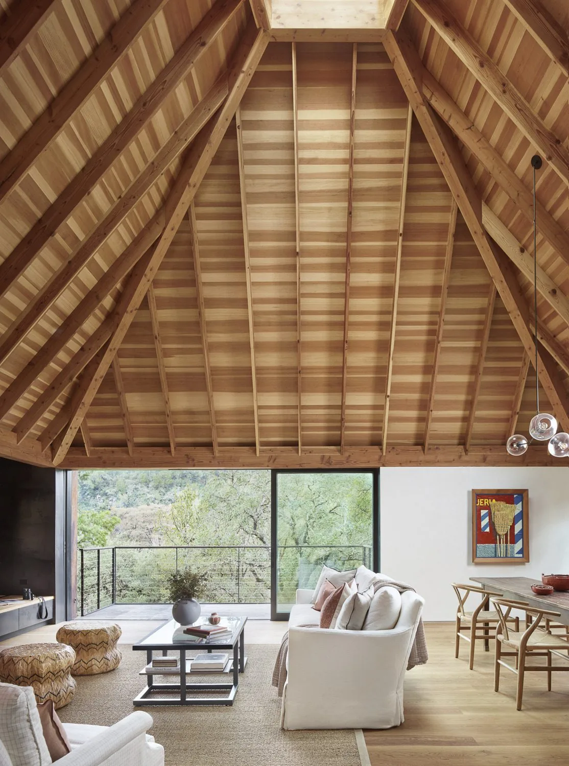 Living and dining area with exposed wood A-frame ceiling and large sliding glass door to balcony at River Bend Residence.