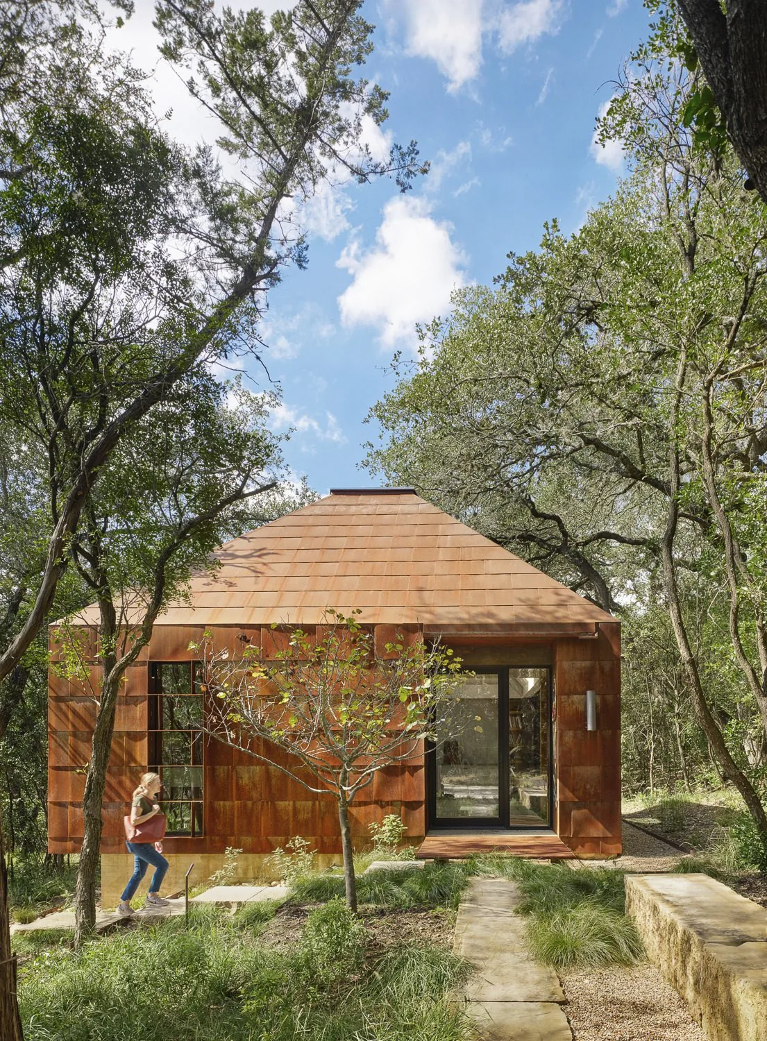 The River Bend Residence features rust-colored panel cladding enveloping a compact structure surrounded by trees.